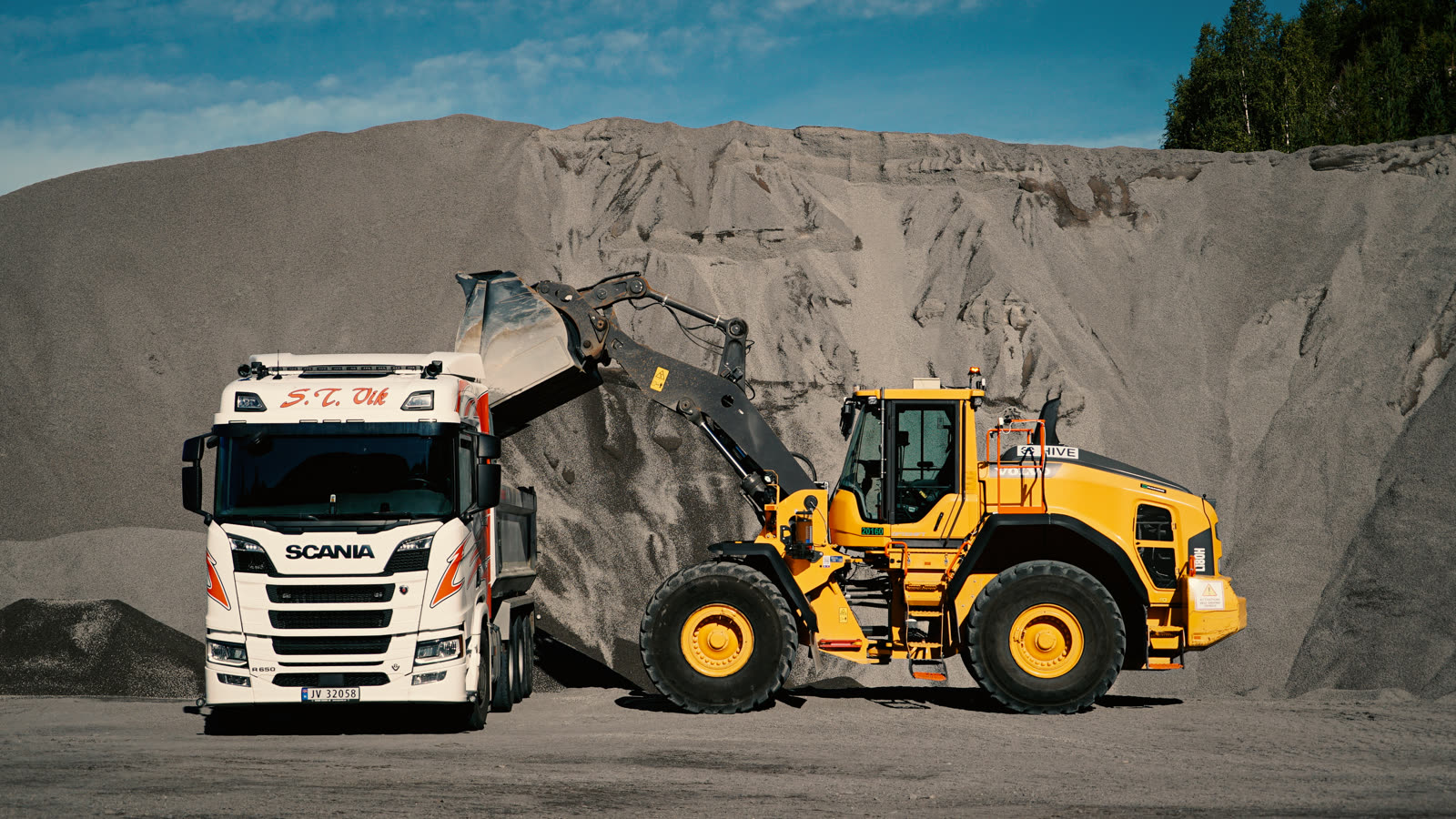 Autonomous Hive-equipped Volvo loader loading a Scania truck at a gravel pit